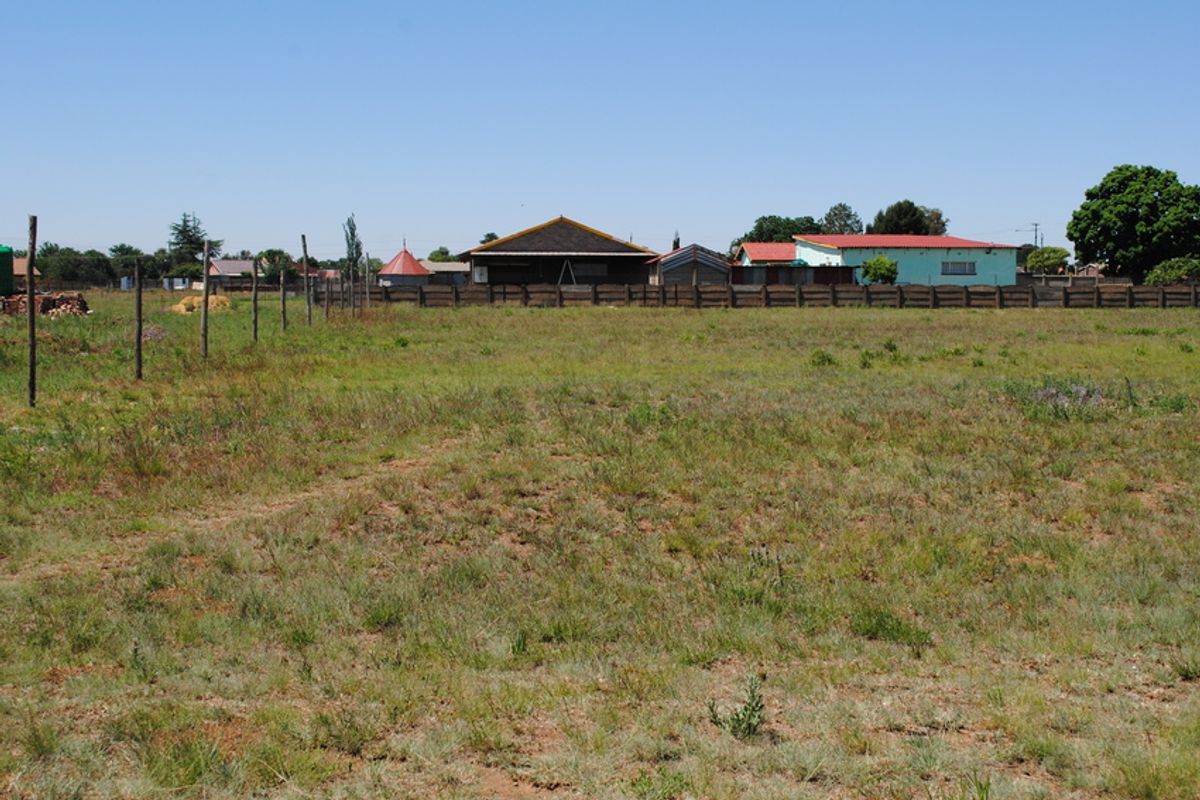 A view of a vacant residential plot featuring open grass land and perimeter fencing.