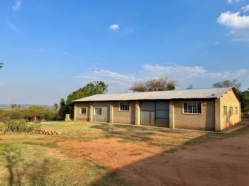 A rear view of a farm building featuring face brick construction, a corrugated metal roof, and large sliding metal access doors.