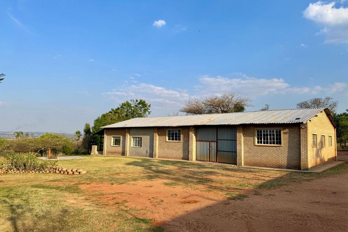 A rear view of a farm building featuring face brick construction, a corrugated metal roof, and large sliding metal access doors.