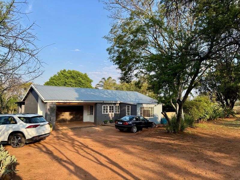 Front view of a farm-style residence featuring a corrugated metal roof, integrated garage, and established trees on a large rural plot.