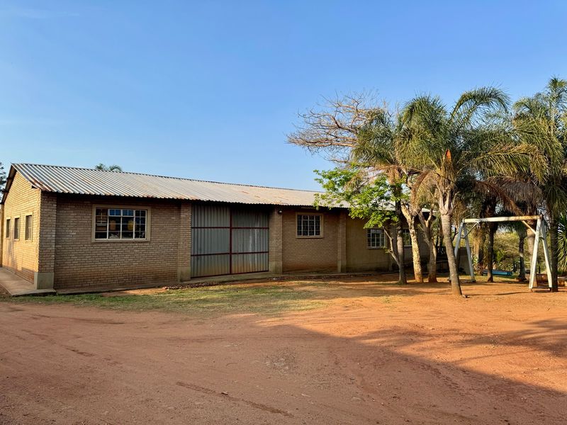 A view of a brick farm building featuring a corrugated metal roof and large sliding metal doors, set in a rural landscape.