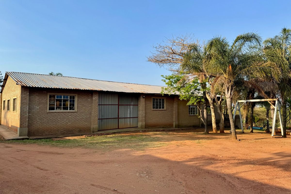 A view of a brick farm building featuring a corrugated metal roof and large sliding metal doors, set in a rural landscape.