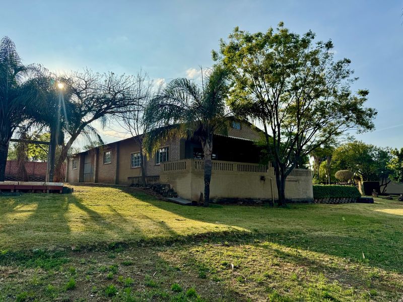 Rear view of a brick farmhouse featuring a covered patio area, established trees, and a spacious surrounding lawn.