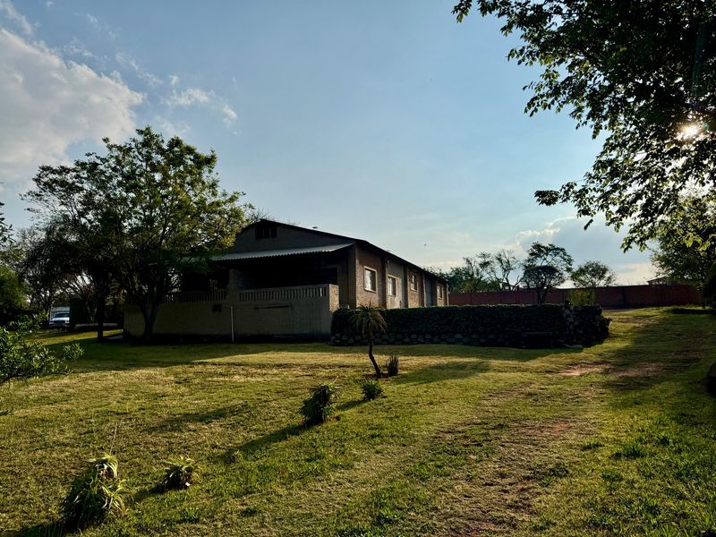 A view of the rear of the farm dwelling featuring a brick facade, covered patio area, and stone retaining wall set within a large garden.