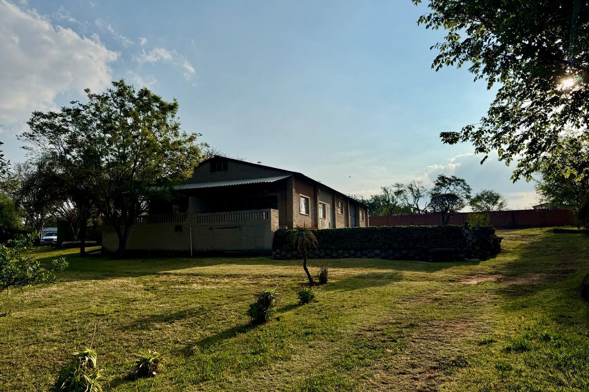 A view of the rear of the farm dwelling featuring a brick facade, covered patio area, and stone retaining wall set within a large garden.
