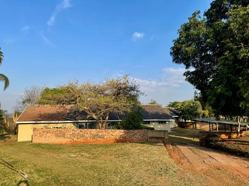 Rear view of the farm property featuring a tiled roof dwelling, brick boundary wall, and a paved driveway leading to a carport area.