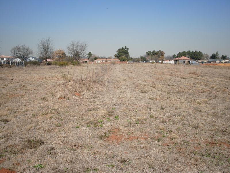A wide-angle view of a vacant residential plot featuring dry grass and surrounding neighborhood infrastructure.