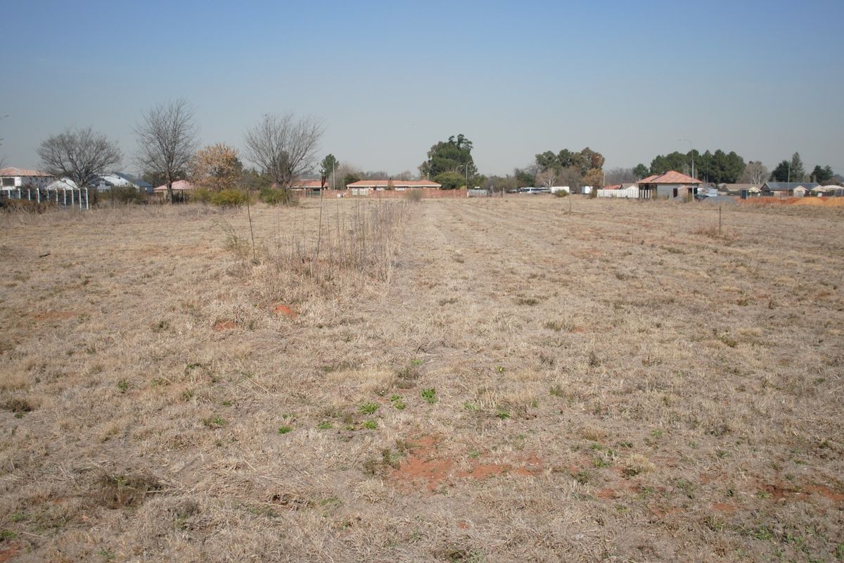 A wide-angle view of a vacant residential plot featuring dry grass and surrounding neighborhood infrastructure.