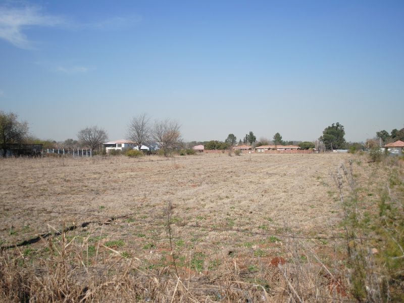 A wide-angle view of a vacant residential plot featuring dry grass and perimeter wire fencing, situated in a suburban neighborhood.