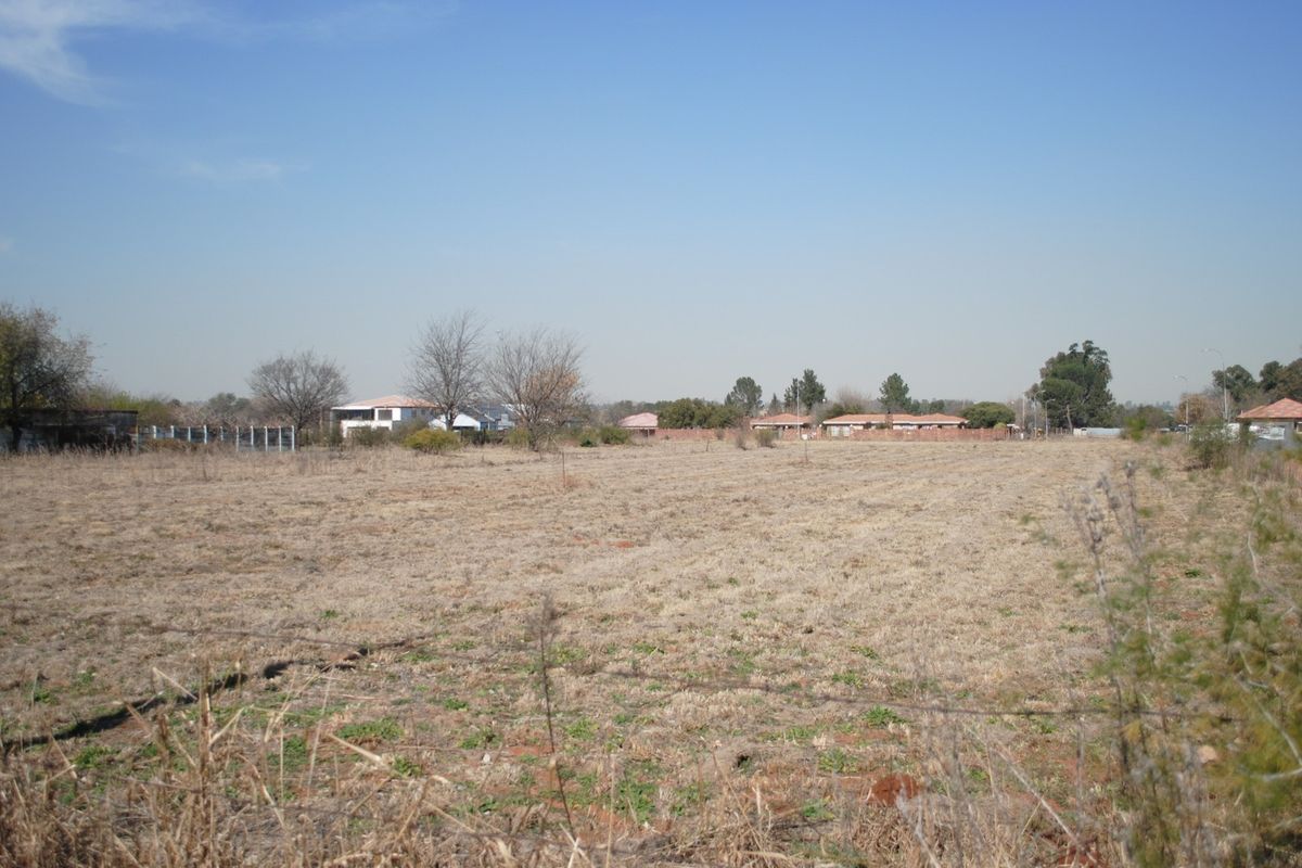 A wide-angle view of a vacant residential plot featuring dry grass and perimeter wire fencing, situated in a suburban neighborhood.