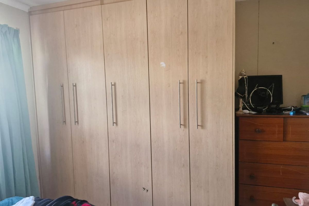 A bedroom featuring floor-to-ceiling built-in wooden wardrobes with modern metal handles.
