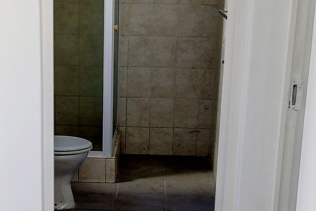 A functional bathroom featuring a shower enclosure and toilet, finished with tiled walls and flooring, currently in need of cosmetic updates and deep cleaning.