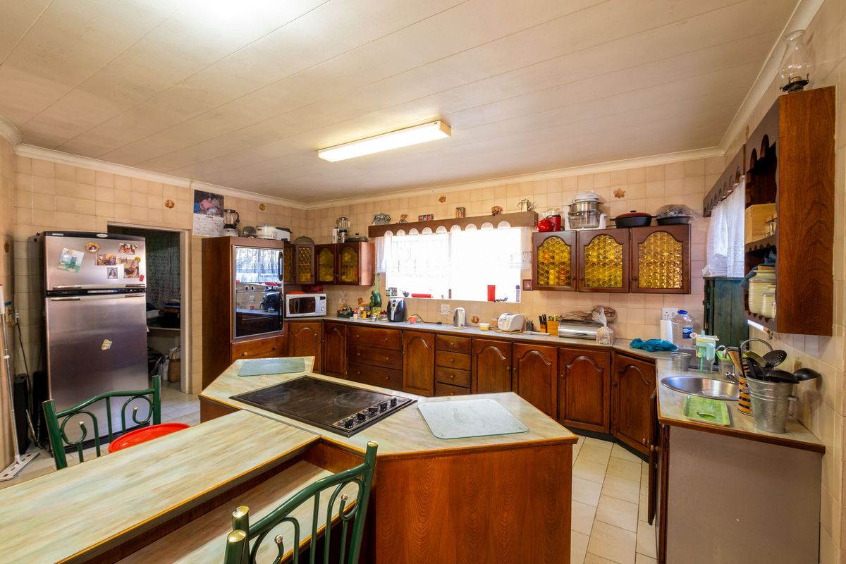 A traditional kitchen featuring extensive wooden cabinetry, laminate countertops, an integrated electric cooktop, and tiled wall finishes, offering significant potential for modernization.