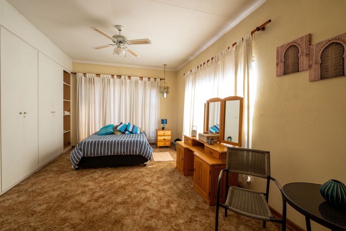 Spacious bedroom featuring built-in cupboards, a ceiling fan, and large windows with natural light, offering a comfortable and functional living space.