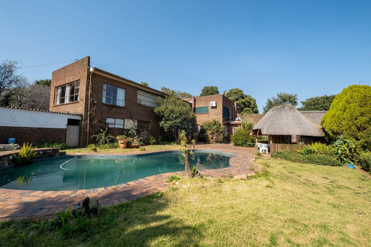 Rear exterior view featuring a swimming pool, brick paved surround, and a traditional thatch lapa set within a garden area.