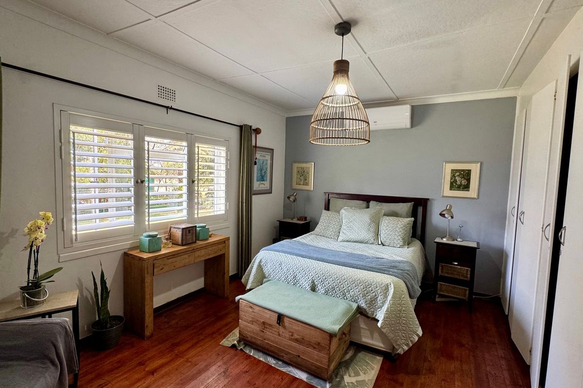 A well-maintained bedroom featuring warm wooden flooring, white plantation shutters, a split-system air conditioning unit, and built-in wardrobe storage.