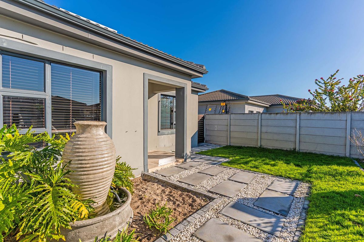 A well-maintained rear exterior view featuring a paved walkway, manicured lawn, and a secure precast concrete boundary wall.