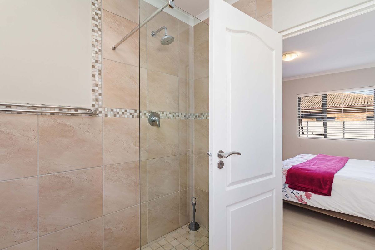 A clean, modern bathroom featuring a walk-in shower with glass screen, neutral wall tiles, and a decorative mosaic border.