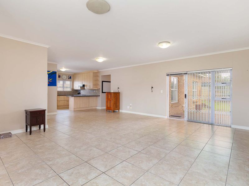 Spacious open-plan living area featuring tiled floors, neutral walls, and an adjoining kitchen with built-in cabinetry, leading to an outdoor patio through sliding doors.