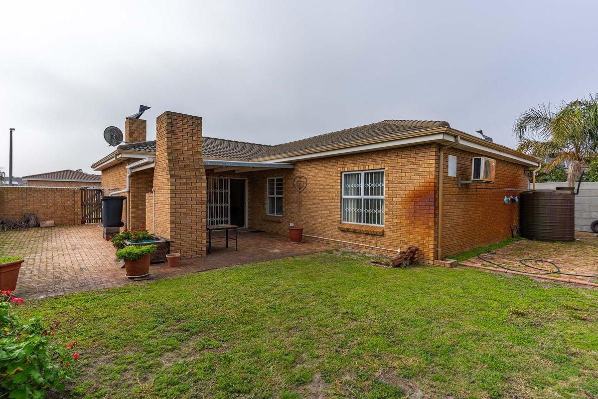 Rear view of a brick house featuring a paved patio area, a chimney, security bars on windows, and a water tank in the garden.
