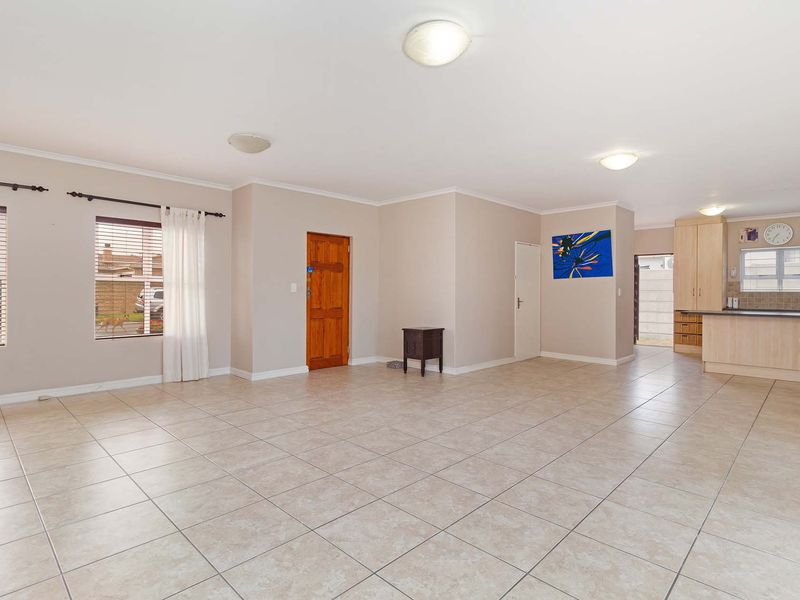 Spacious open-plan living area featuring tiled flooring, neutral walls, and an integrated kitchen with breakfast bar and timber cabinetry.