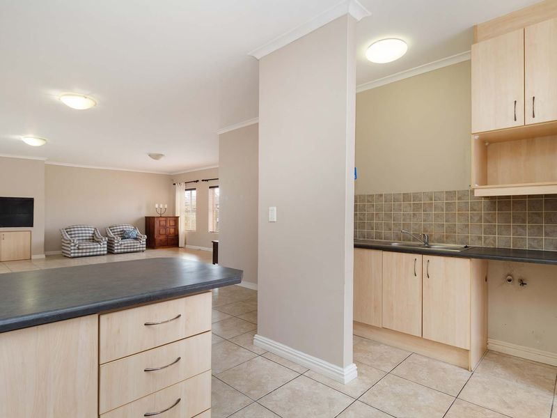 Open plan living area featuring a functional kitchen with laminate cabinetry, tiled backsplash, and tiled flooring, flowing into a spacious living room.