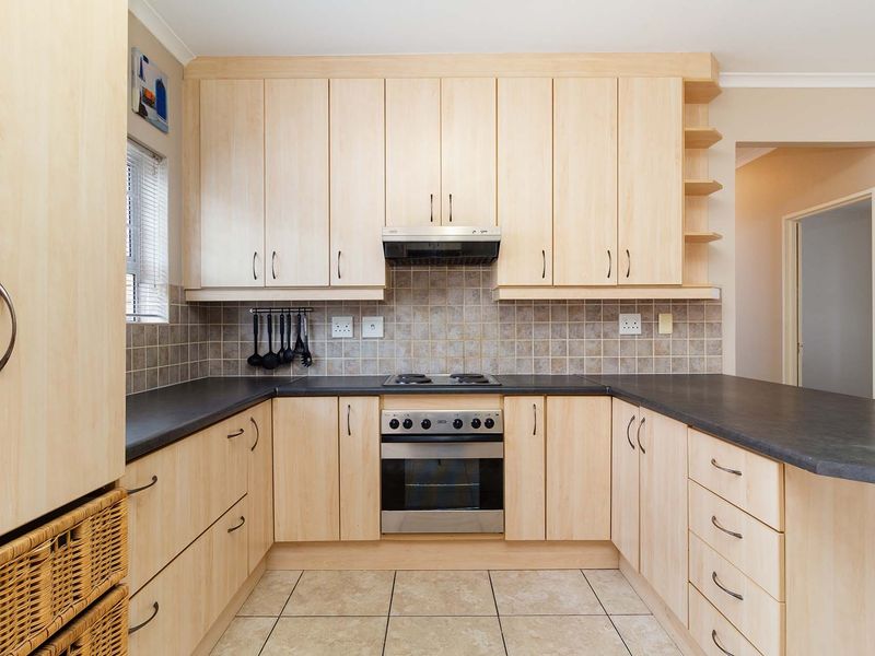 A functional kitchen featuring light wood-finish cabinetry, dark laminate countertops, a built-in oven with gas hob, and neutral tiled flooring and backsplash.