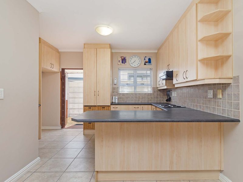 A functional kitchen featuring light wood-finish cabinetry, dark laminate countertops, tiled backsplash, and ceramic floor tiles, offering a clean and practical workspace.