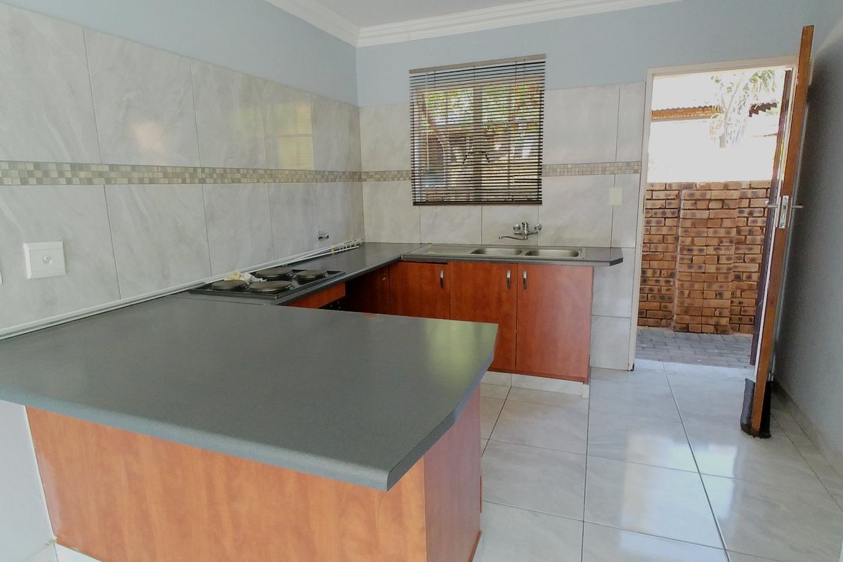 A functional kitchen featuring wooden cabinetry, dark countertops, a built-in hob, and tiled flooring with direct access to an outdoor area.