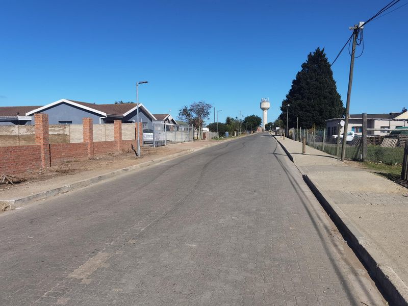A view of the residential street showing paved road, sidewalks, and surrounding boundary walls with a water tower in the distance.