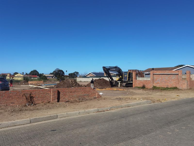 A construction site showing an active excavation area with heavy machinery and partially completed brick boundary walls.