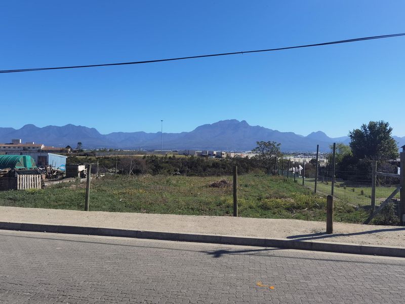 A view of the surrounding landscape and distant mountains from the street level, featuring a vacant plot with wire fencing.