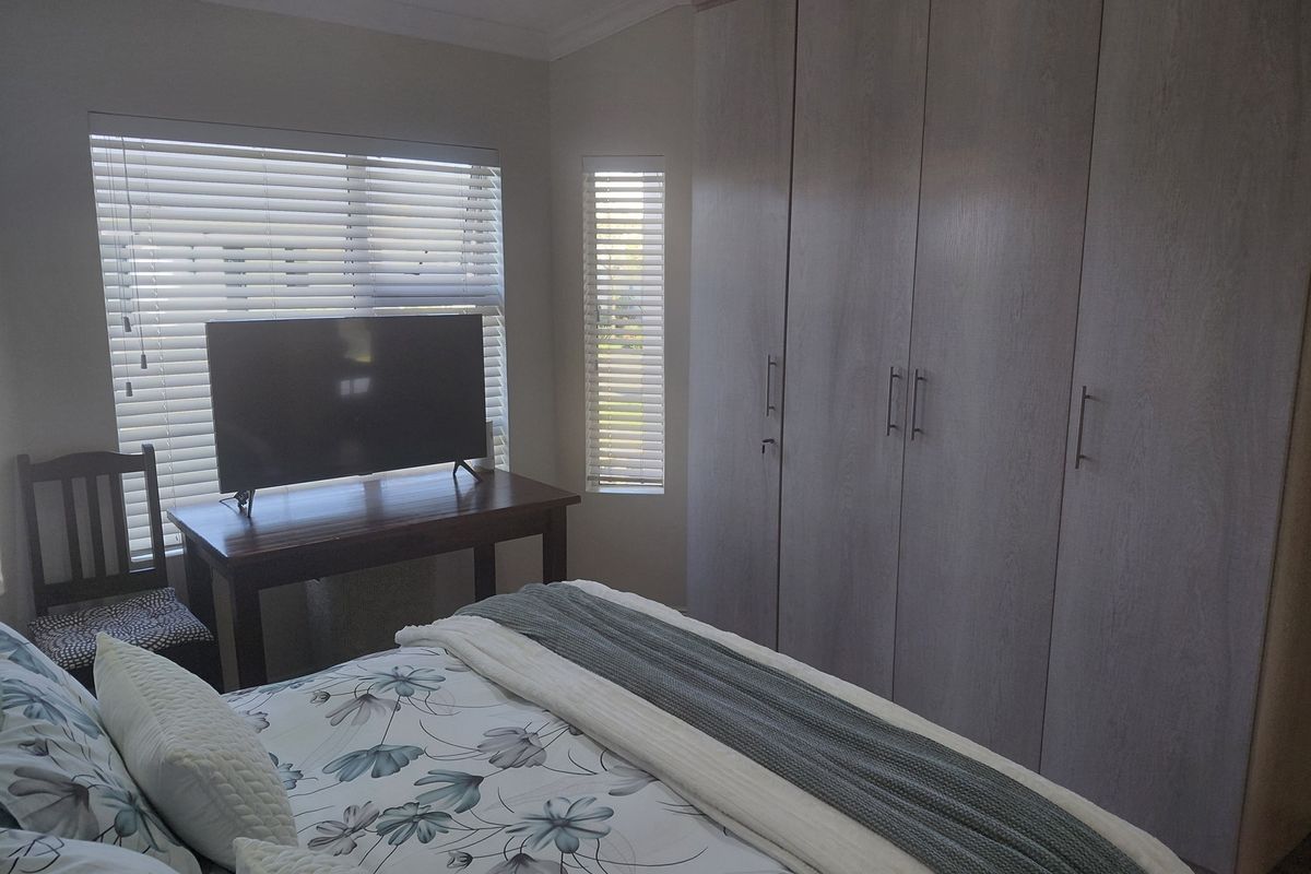 A well-maintained bedroom featuring neutral-toned built-in wardrobes, venetian blinds, and decorative ceiling cornicing.