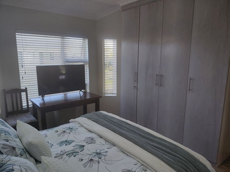 A well-maintained bedroom featuring neutral-toned built-in wardrobes, venetian blinds, and decorative ceiling cornicing.