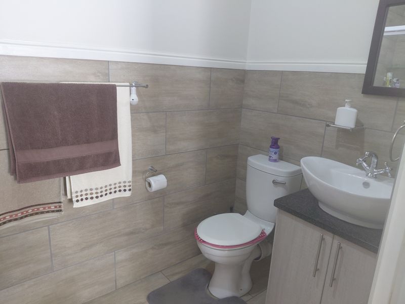 A modern bathroom featuring wood-look ceramic wall tiles, a vanity cabinet with a vessel sink, and a standard toilet.