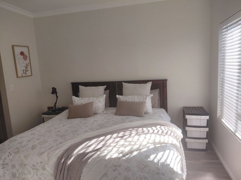 A well-lit bedroom featuring neutral wall tones, crown molding, and modern laminate flooring, complemented by adjustable venetian blinds for natural light control.