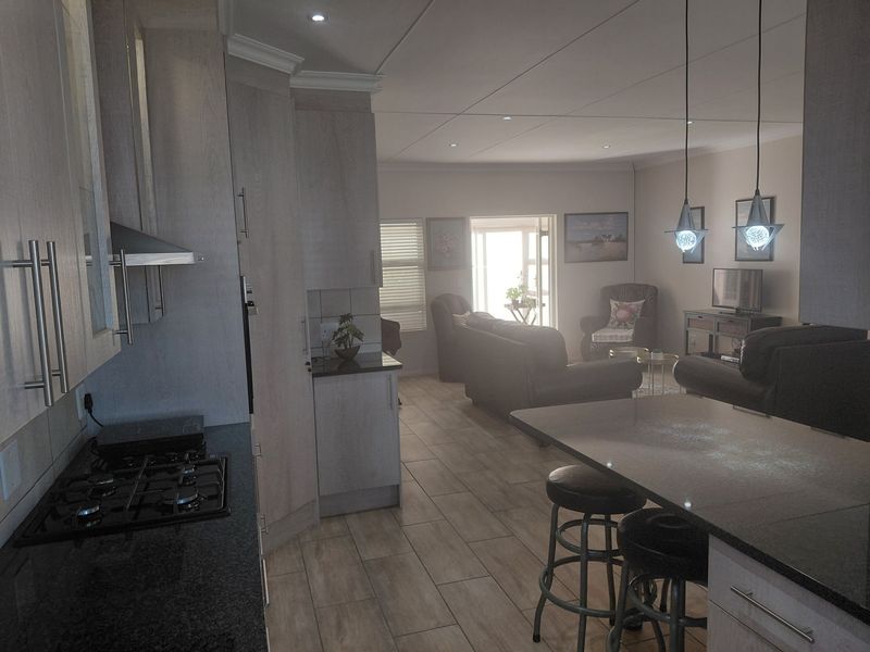 Open-plan kitchen and living area featuring modern cabinetry, granite countertops, gas hob, and tiled flooring with integrated lighting throughout.