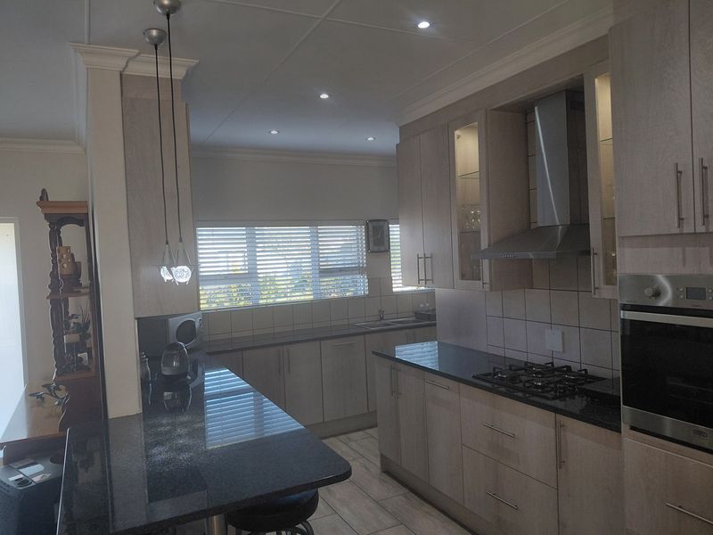 Modern kitchen featuring granite countertops, built-in oven, gas hob, stainless steel extractor fan, and ample cabinetry with a breakfast bar.
