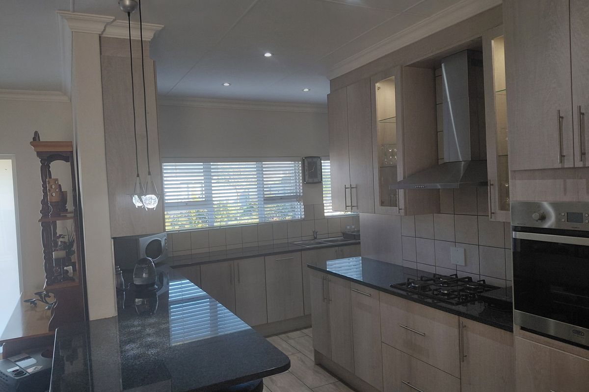 Modern kitchen featuring granite countertops, built-in oven, gas hob, stainless steel extractor fan, and ample cabinetry with a breakfast bar.