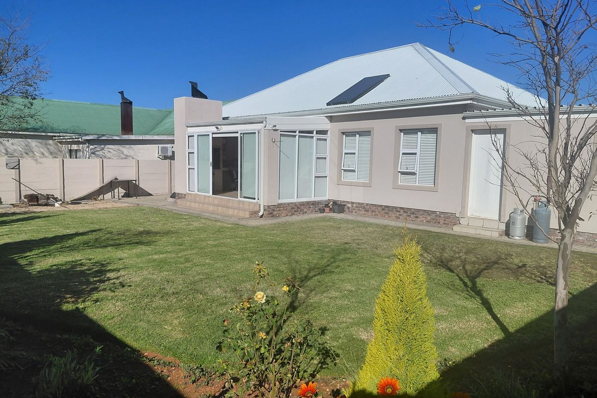 Rear view of the property featuring a well-maintained lawn, corrugated metal roof with solar panel, and sliding glass doors leading to the interior.