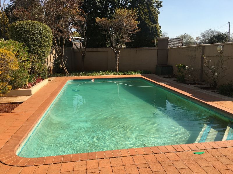 Outdoor swimming pool area featuring a paved surround and perimeter boundary wall, requiring maintenance to the pool water and surface finishes.