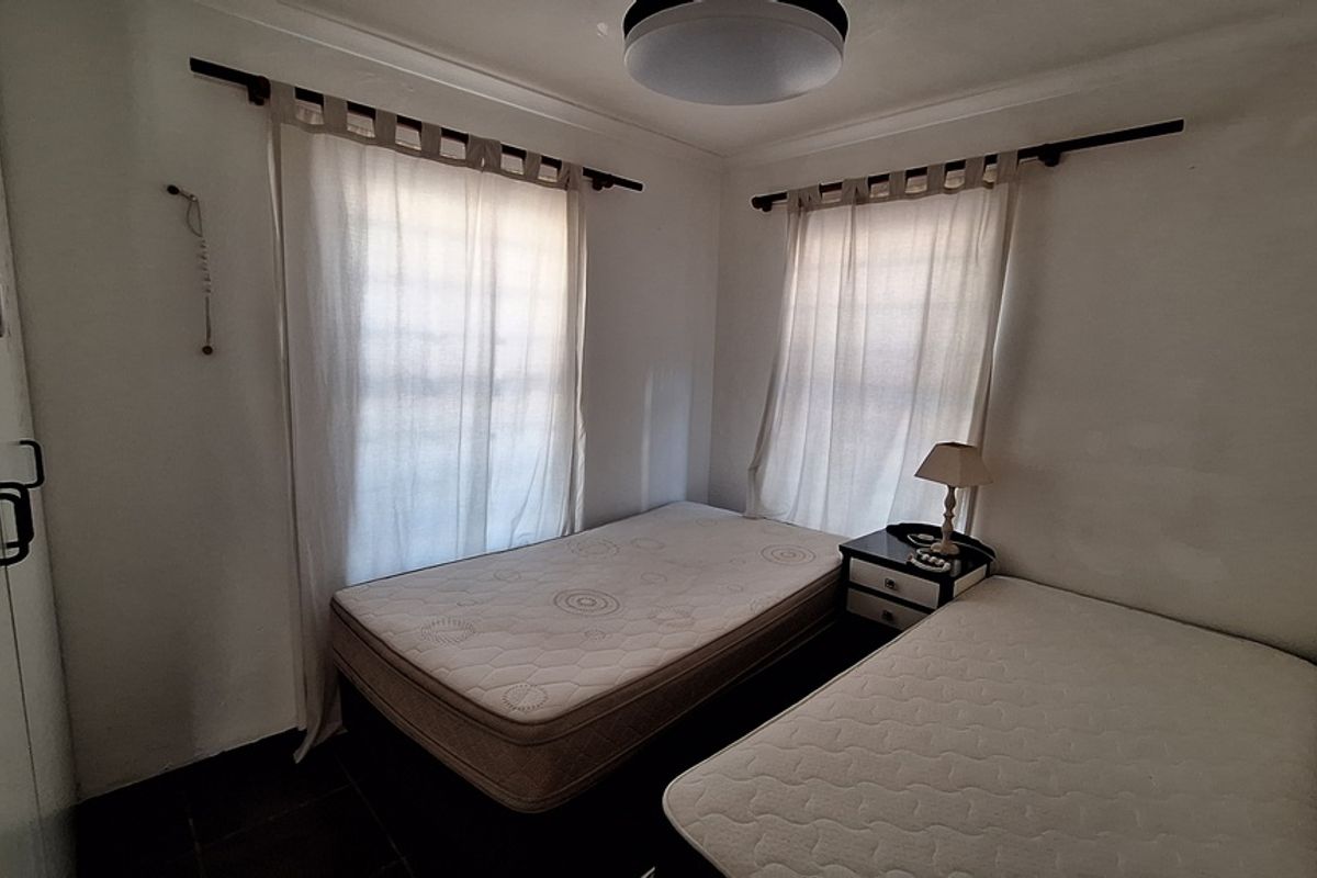 A compact bedroom featuring a built-in wardrobe and dual windows, providing a functional space with neutral finishes.