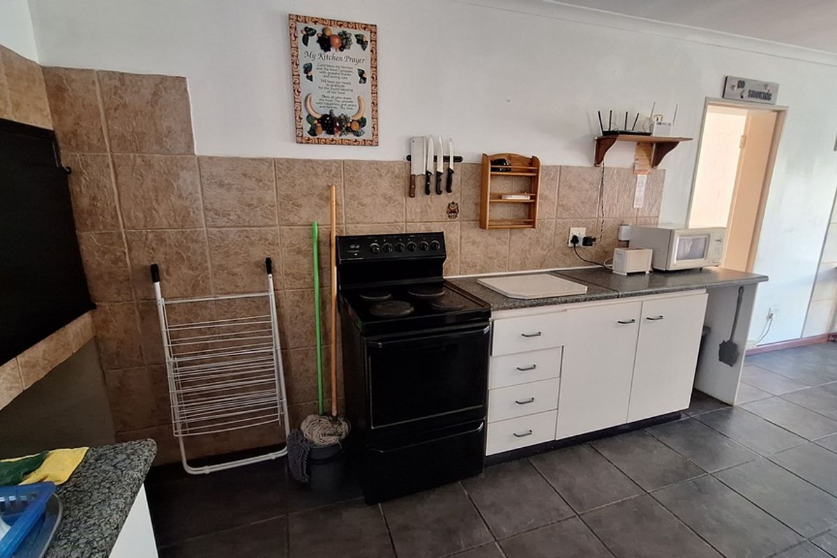 A functional kitchen featuring tiled backsplash, laminate countertops, built-in cabinetry, and a freestanding electric stove with tiled flooring throughout.
