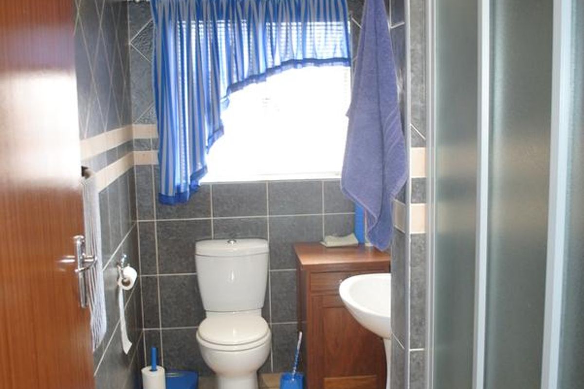 A functional bathroom featuring a shower enclosure, pedestal washbasin, toilet, and tiled finishes throughout.