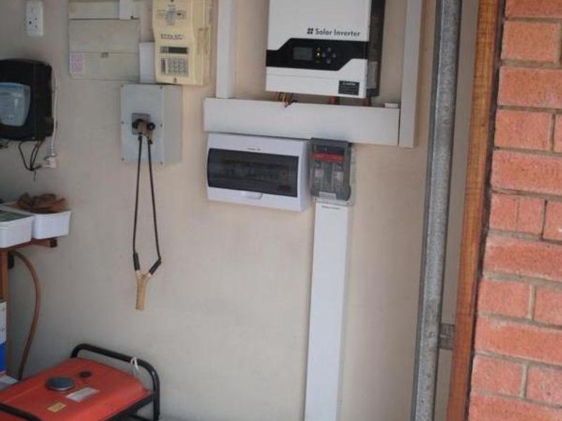 Utility area featuring a wall-mounted solar inverter, electrical distribution board, and battery storage system installed on a tiled floor.