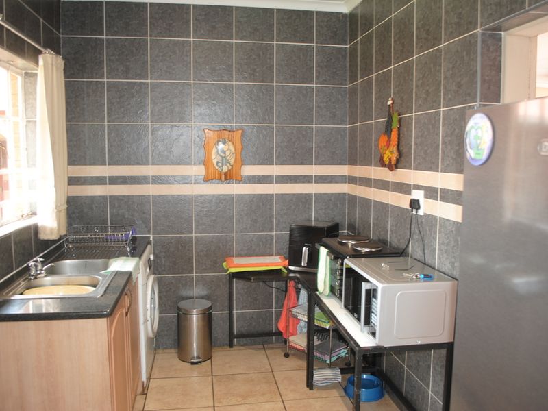 A functional scullery area featuring dark tiled walls, a stainless steel sink, and tiled flooring, providing practical space for food preparation and laundry tasks.