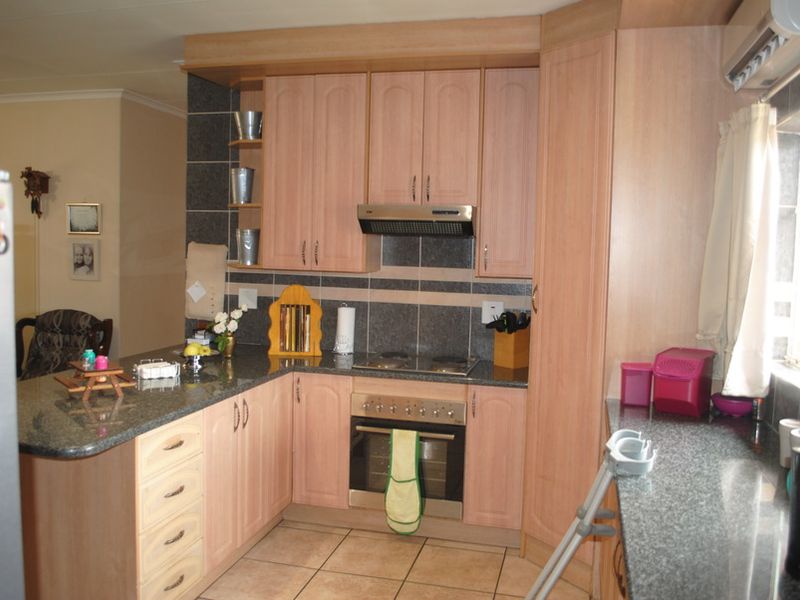 Functional kitchen featuring laminate cabinetry, granite countertops, built-in oven, electric hob, and tiled splashback with an integrated breakfast bar area.