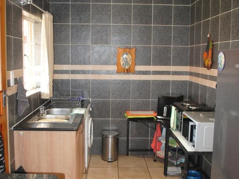 A functional scullery area featuring dark tiled walls, granite countertops, a built-in sink, and tiled flooring, providing additional utility and prep space.
