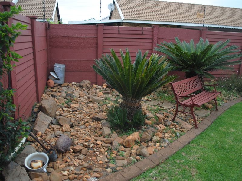 A private rear garden featuring a rock landscaping bed, established cycad plants, and a secure precast boundary wall with electric fencing.