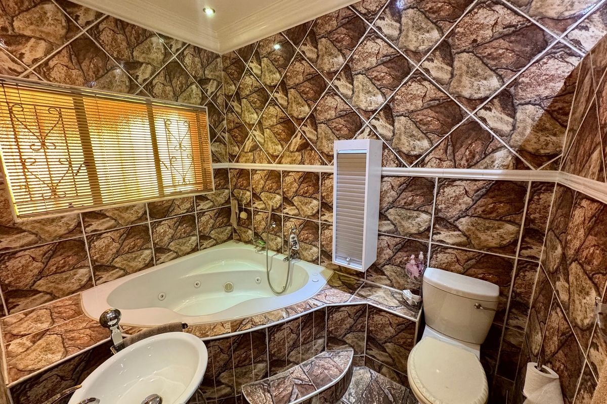 A bathroom featuring a corner jetted bathtub, pedestal basin, and toilet, finished with distinctive stone-effect ceramic wall and floor tiling.